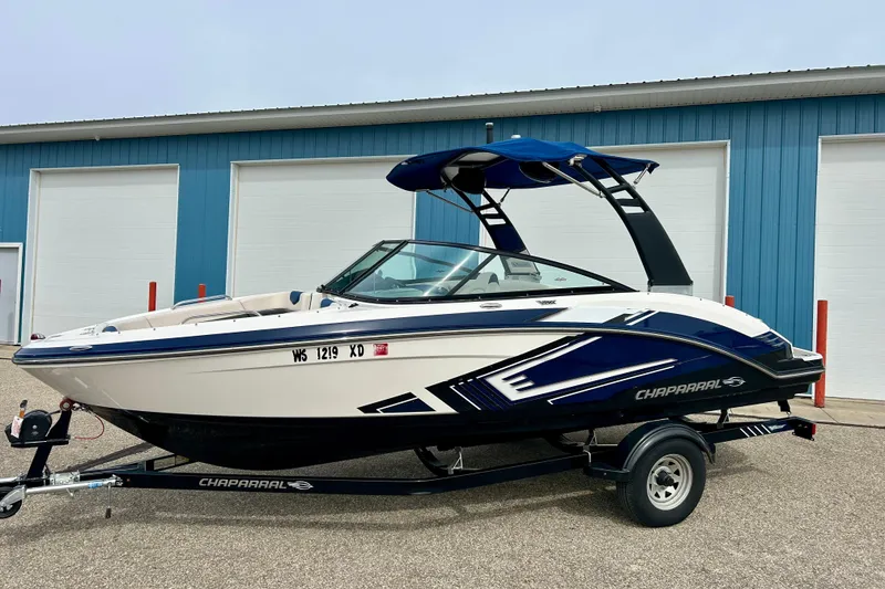 Slide: The Image of 2017 Chaparral 203 Vortex boat with blue accents on a trailer, parked near a blue building. - 7