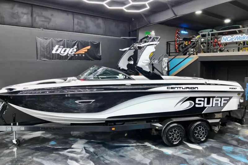 The Image of 2017 Centurion Ri237 surf boat displayed indoors on a trailer. - 0