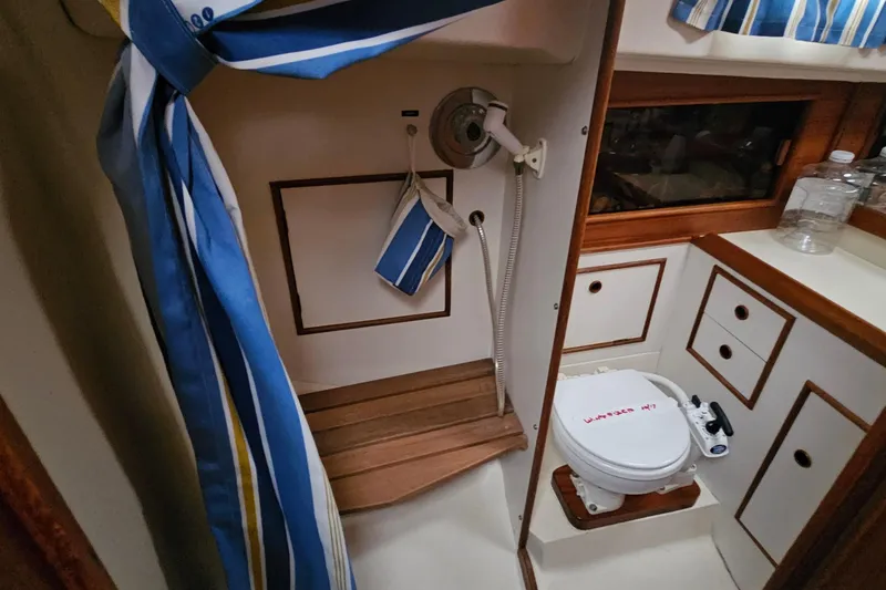 Slide: The Image of 1985 Nonsuch 30 sailboat bathroom with striped curtain, wooden accents, and compact toilet. - 13