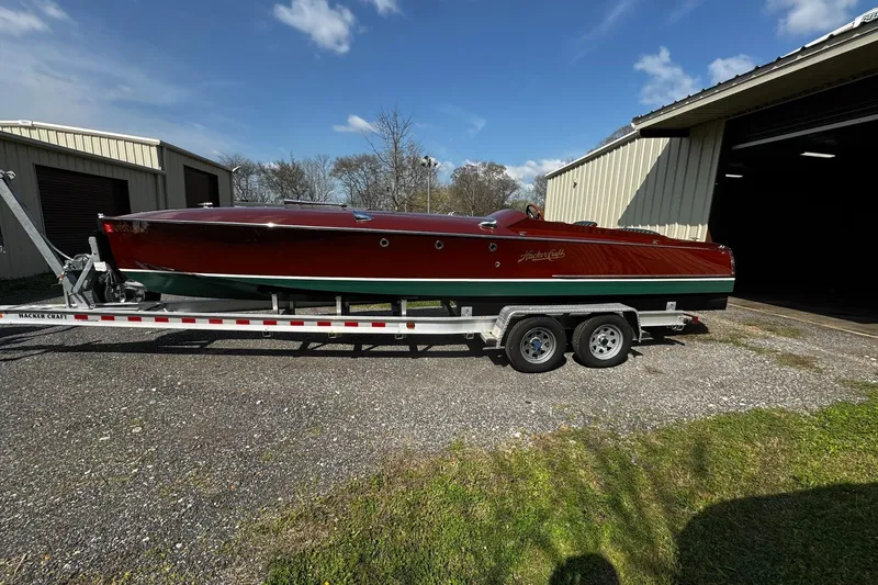 The Image of 2014 Hacker-Craft 26' Runabout on trailer, parked outside a garage under a clear sky. - 0