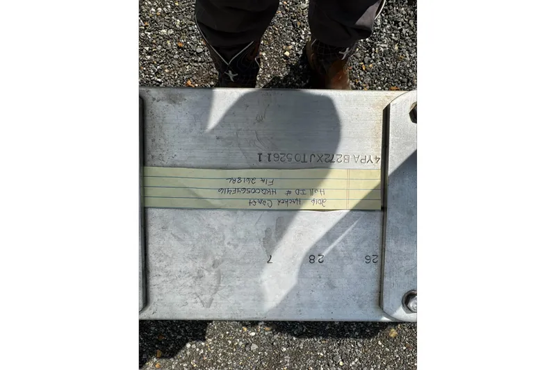 Slide: The Image of Metal plate with engraved text, shadow, and handwritten note on gravel surface. - 24