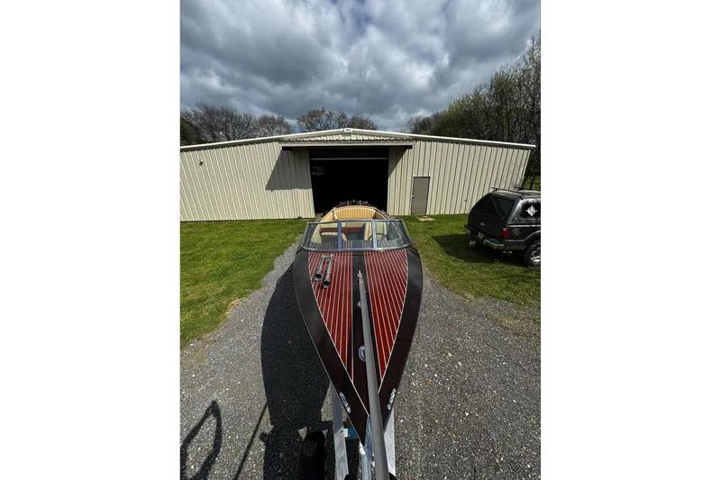 Slide: The Image of 2016 Hacker-Craft 28 Sport boat on trailer outside metal building under cloudy sky. - 8