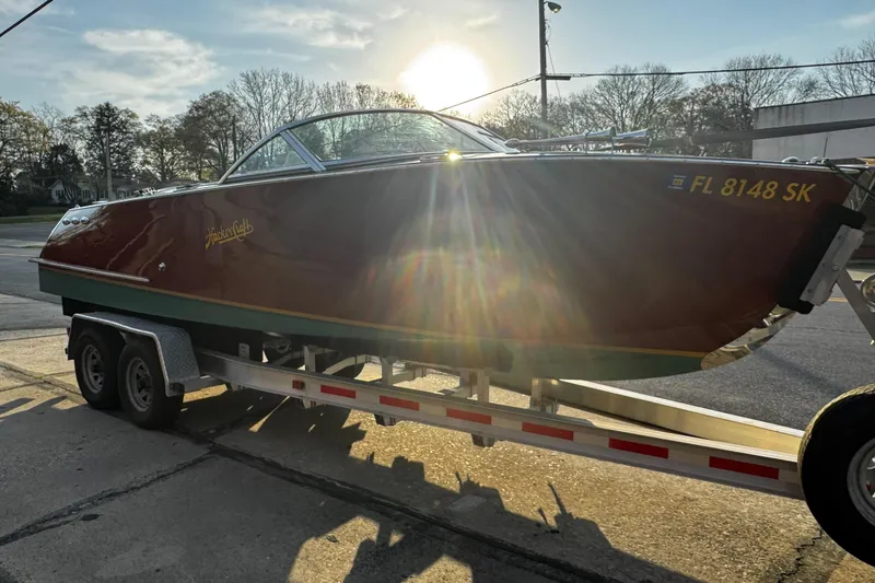 Slide: The Image of 2019 Hacker-Craft 23 Runabout on trailer, sunlit, with trees in background. - 16