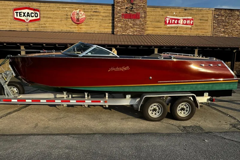 Slide: The Image of 2019 Hacker-Craft 23 Runabout boat on trailer, parked outside rustic building. - 4