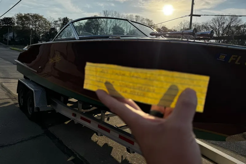 Slide: The Image of 2019 Hacker-Craft 23 Runabout on trailer, hand holding yellow paper, sunset background. - 6