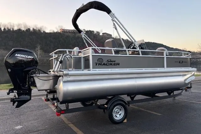 Slide: The Image of 2026 Sun Tracker Bass Buggy 18 DLX pontoon boat on trailer, parked near a lake. - 2