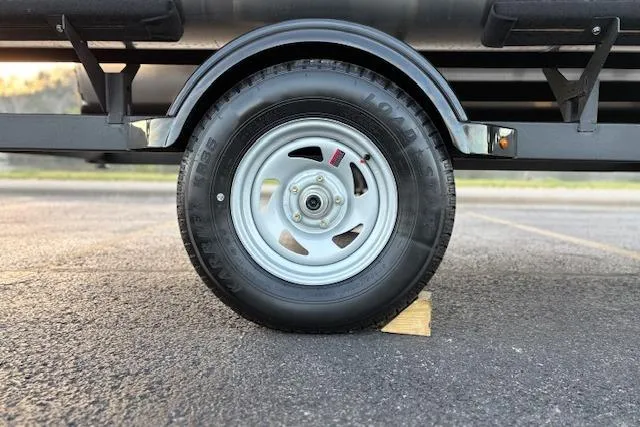 Slide: The Image of 2026 Sun Tracker Bass Buggy 18 DLX trailer wheel on asphalt with wooden chock. - 25