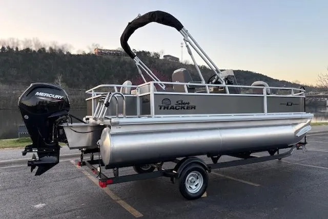 Slide: The Image of 2026 Sun Tracker Bass Buggy 18 DLX pontoon boat with Mercury engine, parked near a scenic lake. - 3