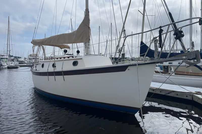 The Image of 1987 Com-Pac 27 sailboat docked in a marina, featuring a beige sail cover. - 0