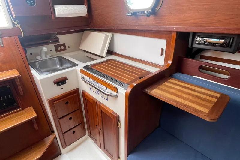 Slide: The Image of 1987 Com-Pac 27 yacht interior with wooden cabinetry, sink, and compact kitchen area. - 19