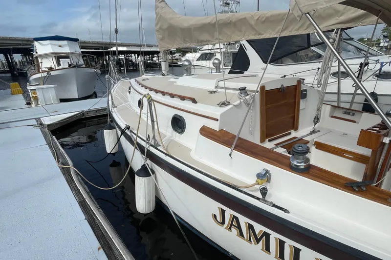 Slide: The Image of 1987 Com-Pac 27 sailboat docked at marina, featuring wooden accents and beige canopy. - 3