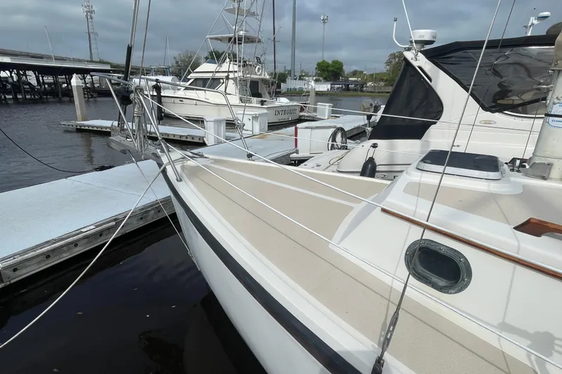 Slide: The Image of 1987 Com-Pac 27 sailboat docked at marina, overcast sky, nearby boats visible. - 4