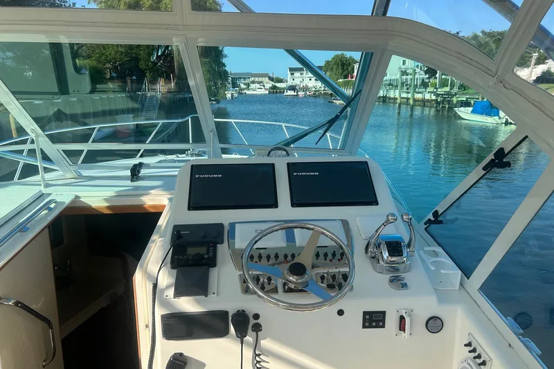 Slide: The Image of Helm of 2012 Cabo 32 Express boat with navigation screens and controls, docked by a serene waterway. - 2