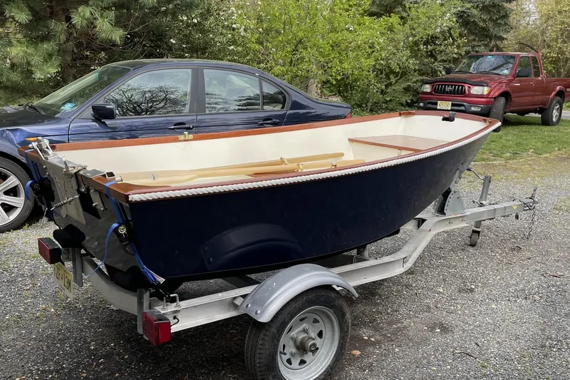 Slide: The Image of Small blue boat on trailer, parked beside cars in a leafy area. - 100