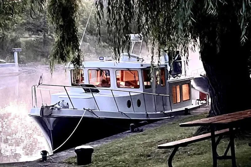 Slide: The Image of 2010 American Tug "34" Pilothouse Trawler docked by a serene riverside under trees. - 114