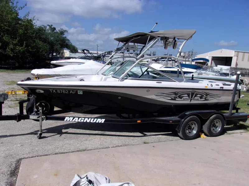 The Image of 2006 Correct Craft SUPER AIR NAUTIQUE 210 TEAM EDITION boat on trailer, parked outdoors. - 1