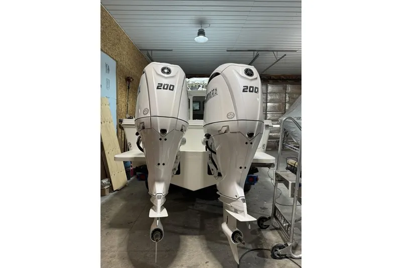 Slide: The Image of 2025 Parker 2420 Sport Cabin with twin 200 horsepower outboard engines in a garage. - 23