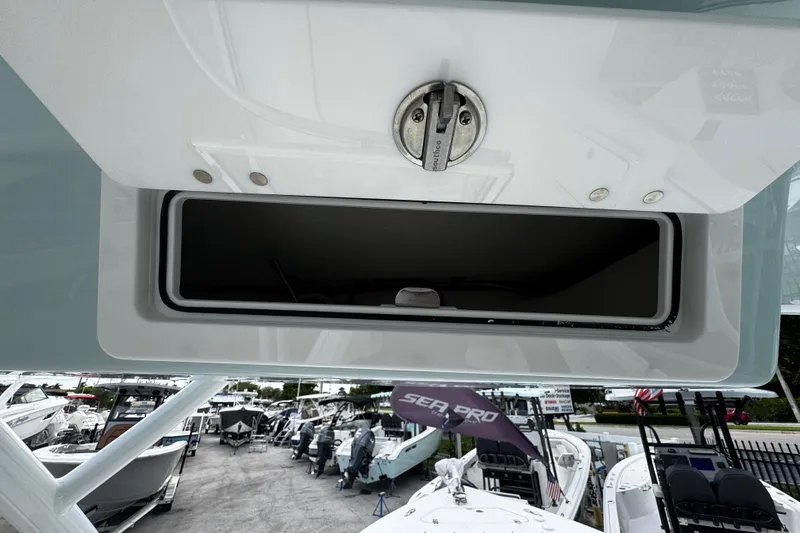 Slide: The Image of 2026 Sea Pro 240 Dual Console boat storage compartment, open lid, marina background. - 17