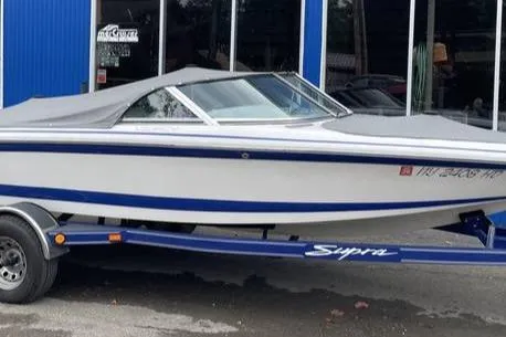 The Image of 2001 Supra Legacy boat on trailer, covered, parked outside a blue building. - 1
