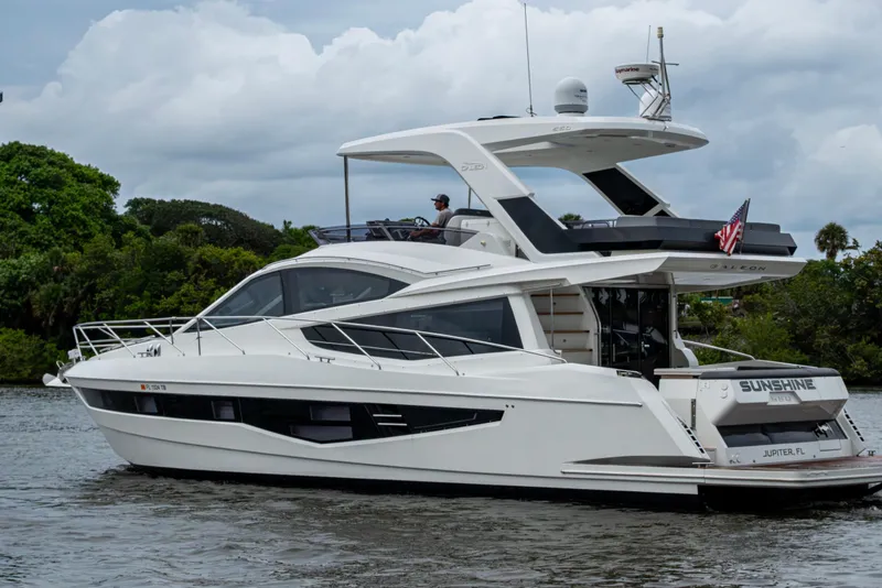 Slide: The Image of 2020 Galeon 550 Fly yacht cruising on a river with lush greenery in the background. - 2