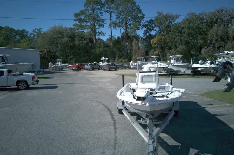 Slide: The Image of 2022 Blazer Bay 2200 boat on trailer in a parking lot with trees and vehicles. - 4