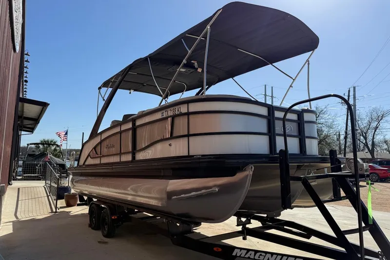 Slide: The Image of 2022 Barletta L23UCA pontoon boat on trailer, parked outdoors under clear sky. - 2