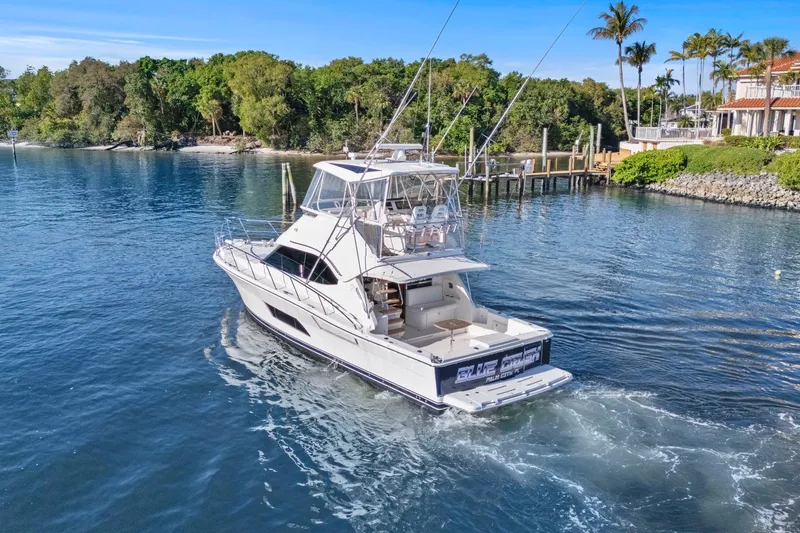 Slide: The Image of 2016 Riviera 43 Open Flybridge yacht cruising near lush shoreline and docks. - 12