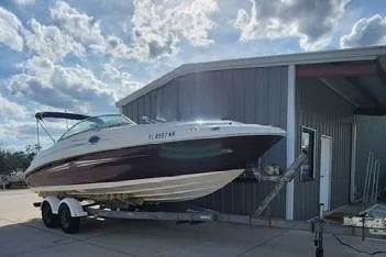 The Image of 2008 Sea Ray 240 Sundeck boat on trailer, parked near a metal building under a cloudy sky. - 1