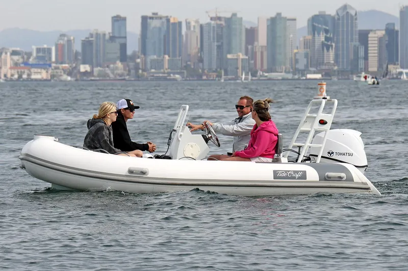 Slide: The Image of Manufacturer Provided Image: 2025 Tide Craft Catalina 13 boat with passengers on water, city skyline in background. - 1