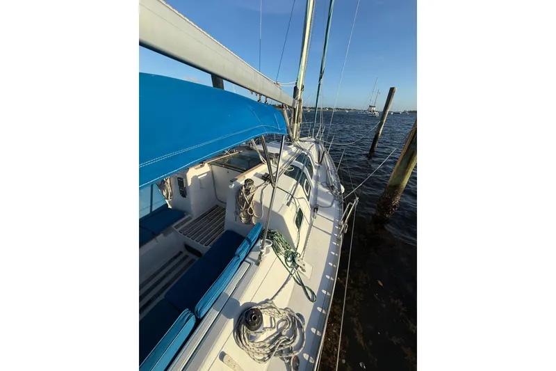 Slide: The Image of 1990 Beneteau First 32s5 sailboat docked, featuring blue canopy and ropes, on calm water. - 15