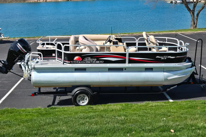 The Image of 2016 Sun Tracker Bass Buggy 18 DLX pontoon boat on trailer by a lake. - 0