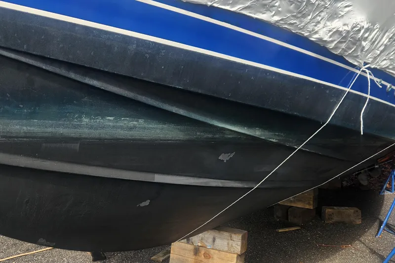 Slide: The Image of 1985 Bertram 33 Flybridge Cruiser hull on wooden blocks, showing blue and black paint. - 10