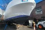 Slide: The Image of 1985 Bertram 33 Flybridge Cruiser boat in dry dock, partially covered, near a brick building. - 9