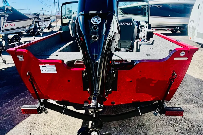 Slide: The Image of 2026 Lund 1650 Angler Sport boat, red exterior, rear view with motor, parked outdoors. - 4