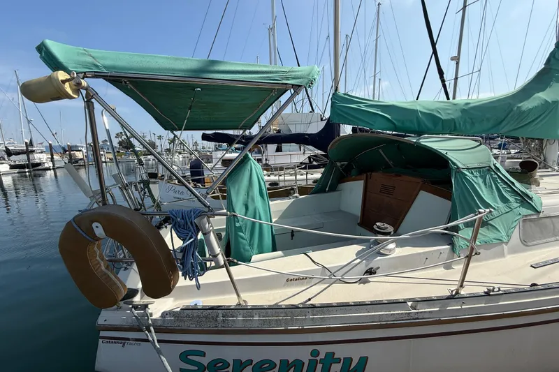 Slide: The Image of 1987 Catalina 36 sailboat docked, featuring green canvas covers and a visible life preserver. - 10