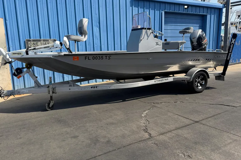 Slide: The Image of 2024 Xpress H190B Bay boat on trailer, parked by blue building. - 3