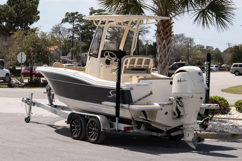 Slide: The Image of 2026 Scout 215 XSF boat on trailer, parked near palm tree in sunny setting. - 4