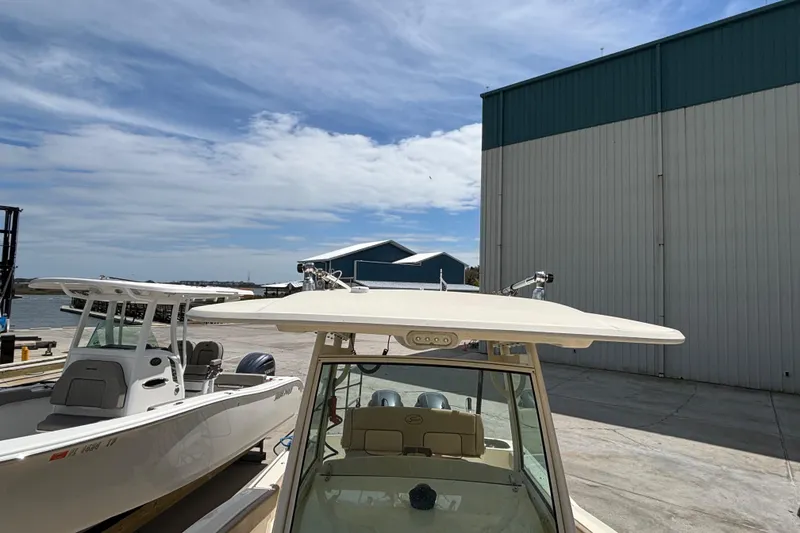 Slide: The Image of 2016 Scout 255 LXF boat docked near a large warehouse under a blue sky. - 22