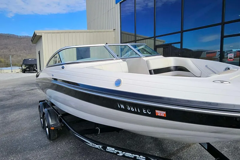 Slide: The Image of 2011 Bryant 210 boat on trailer, parked near a building with reflective windows. - 2