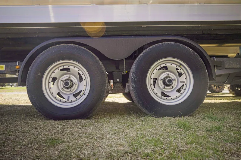 Slide: The Image of 2025 SunCatcher Fusion 324SS trailer wheels on grass, showcasing dual axle design. - 11