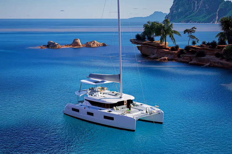 Slide: The Image of 2026 Lagoon 47 catamaran sailing in crystal-clear tropical waters near rocky islands. - 2