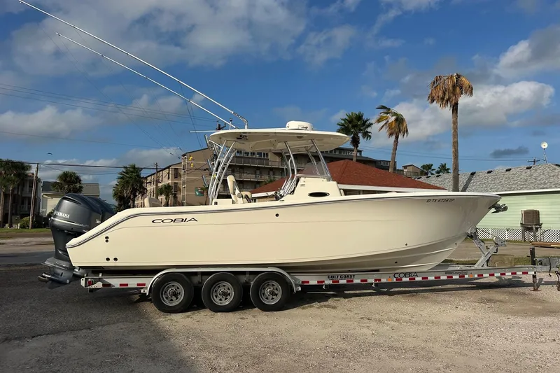 Slide: The Image of 2016 Cobia 296 Center Console boat on trailer, parked outdoors under blue sky. - 3