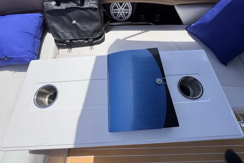 Slide: The Image of Boat interior with table, cup holders, blue folder, and cushions on a 2015 Four Winns H290. - 78
