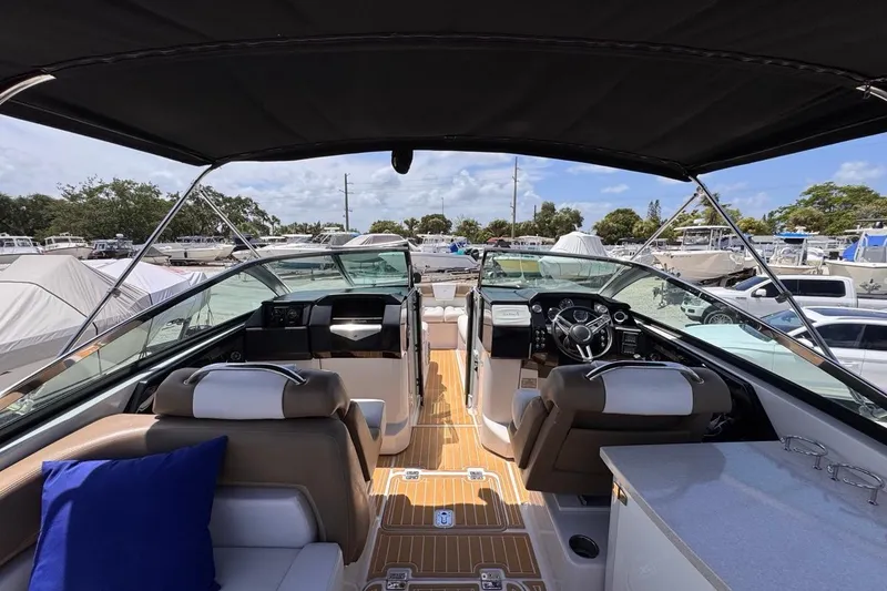 Slide: The Image of 2015 Four Winns H290 boat interior with seating, steering wheel, and canopy at a marina. - 90
