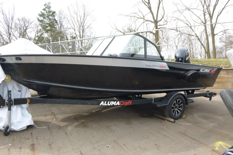 The Image of 2025 Alumacraft Trophy 185X Sport boat on trailer, parked outdoors. - 1