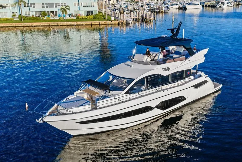 Slide: The Image of 2021 Sunseeker Manhattan 68 yacht cruising on calm waters near a marina. - 2