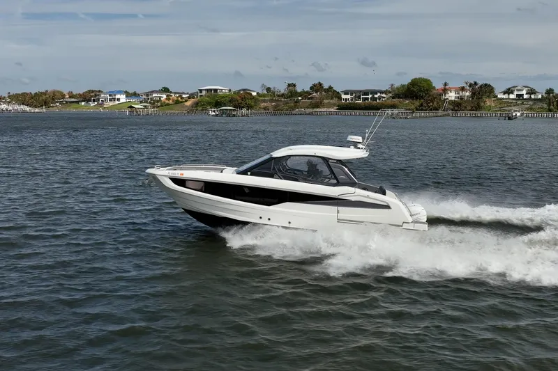 Slide: The Image of 2023 Galeon 325 GTO cruising on a scenic waterway near coastal homes. - 4