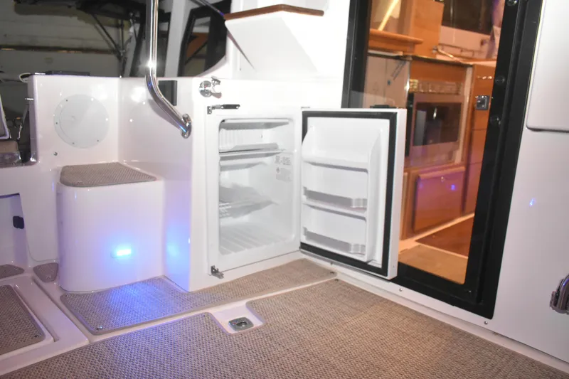 Slide: The Image of 2026 Cutwater C-32 CB boat interior with open mini fridge and carpeted flooring. - 43