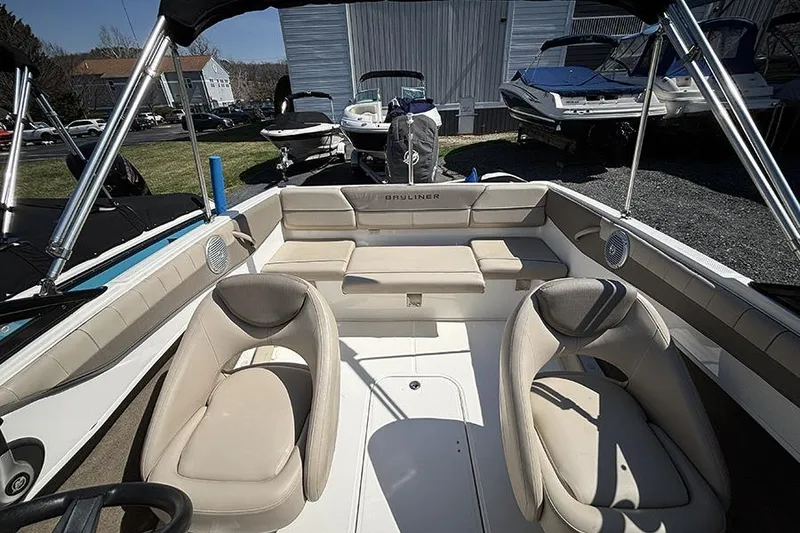 Slide: The Image of 2016 Bayliner 185 Bowrider interior with beige seating and steering wheel, docked outdoors. - 9