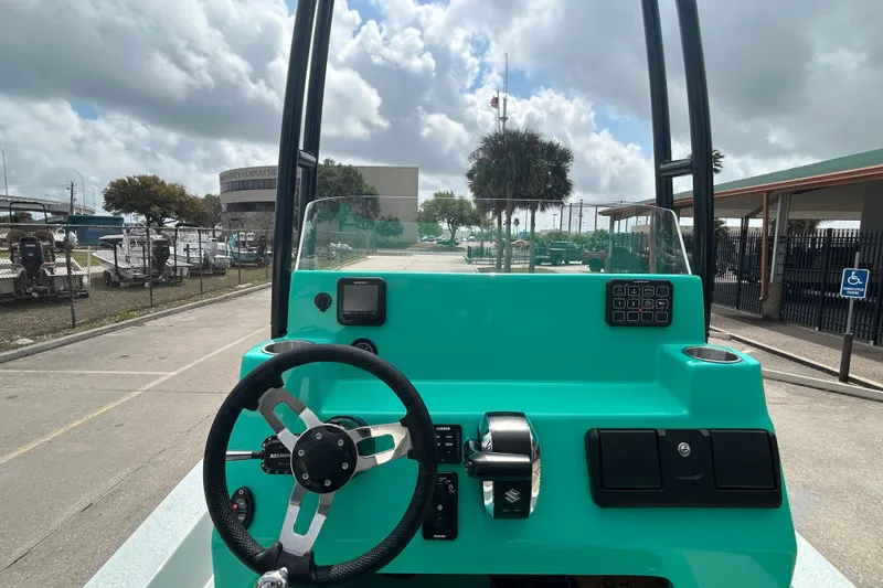 Slide: The Image of 2026 Gulf Coast Saber Cat boat dashboard with steering wheel and controls, under cloudy sky. - 12